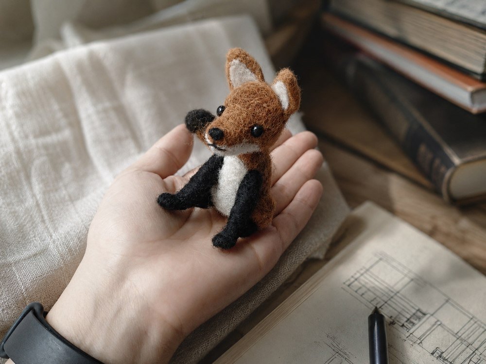 Mano trabajando el detalle de un personaje textil en proceso.